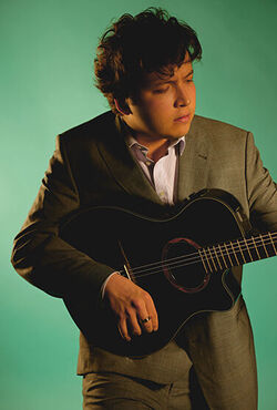 Eine Person in einem braunen Anzug spielt auf einer akustischen Gitarre