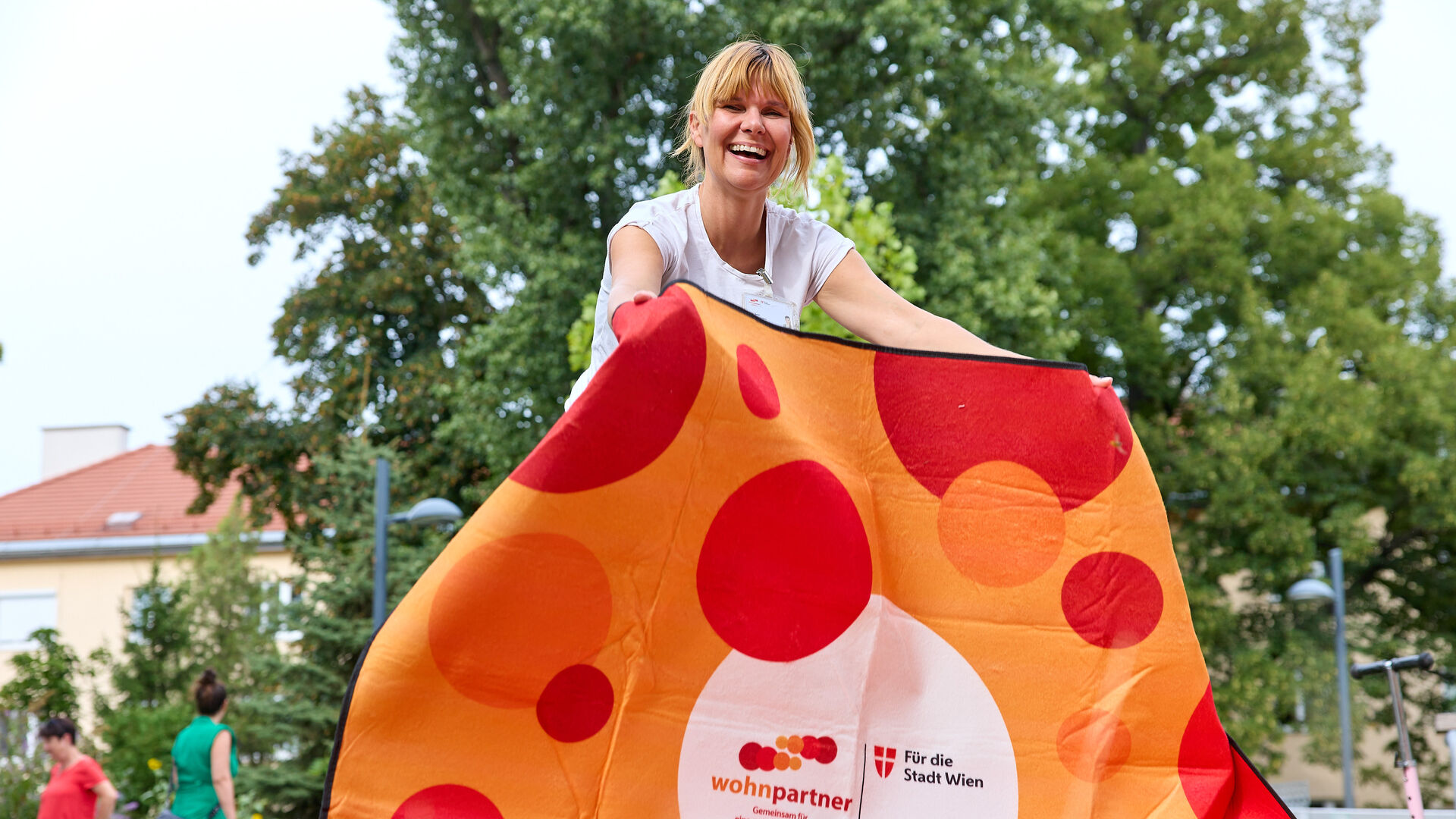 Eine Frau breitet eine Picknickdecke aus, auf der Decke sieht man das wohnpartner-Logo.