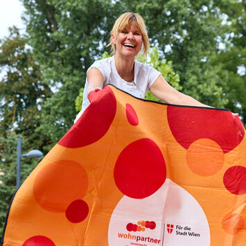 Eine Frau breitet eine Picknickdecke aus, auf der Decke sieht man das wohnpartner-Logo.
