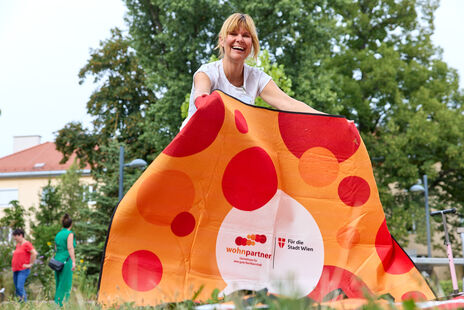 Eine Frau breitet eine Picknickdecke aus, auf der Decke sieht man das wohnpartner-Logo.