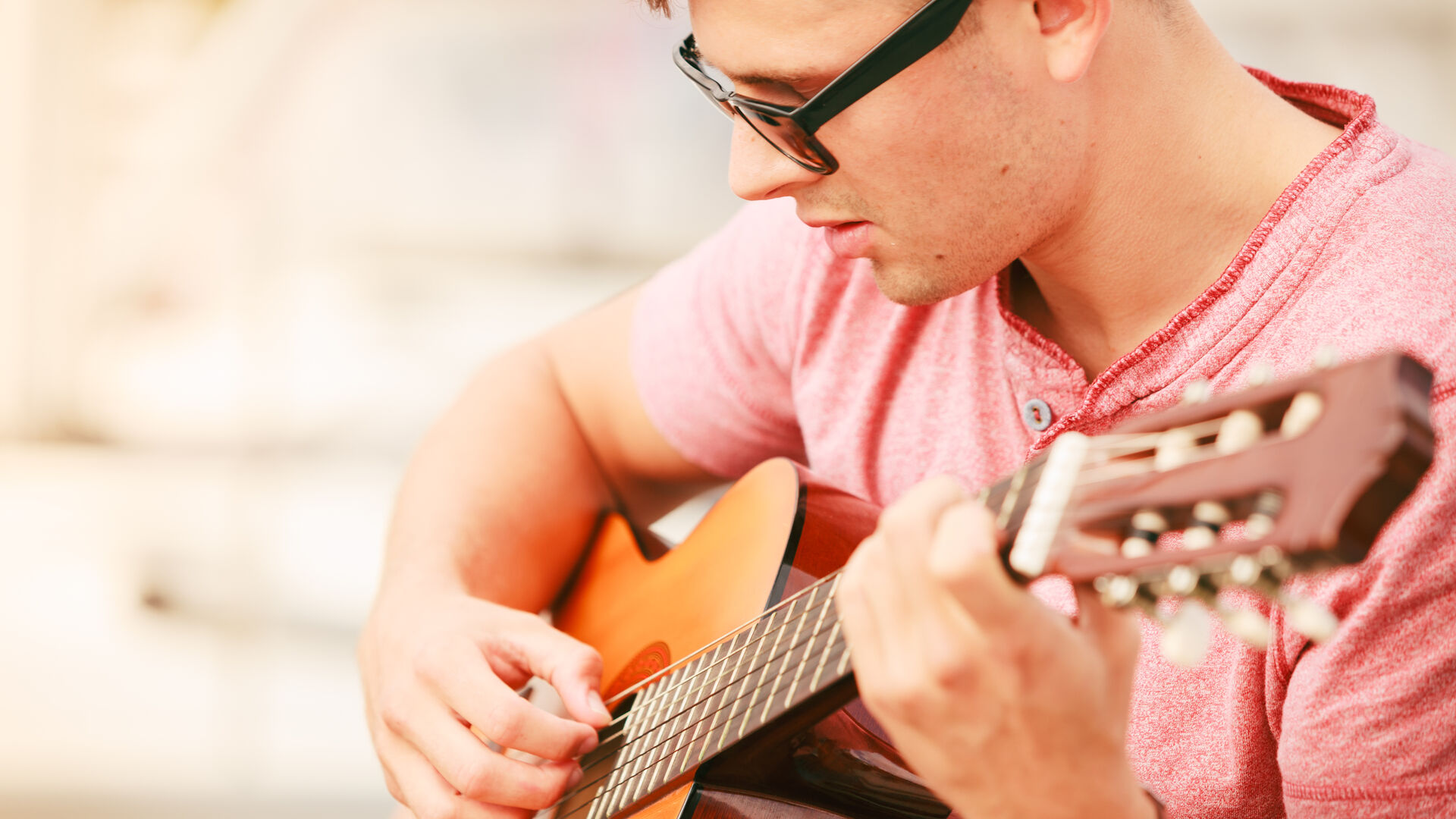 Ein Mann mit Sonnenbrille und rotem Shirt spielt auf einer Gitarre.