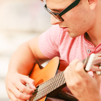 Ein Mann mit Sonnenbrille und rotem Shirt spielt auf einer Gitarre.