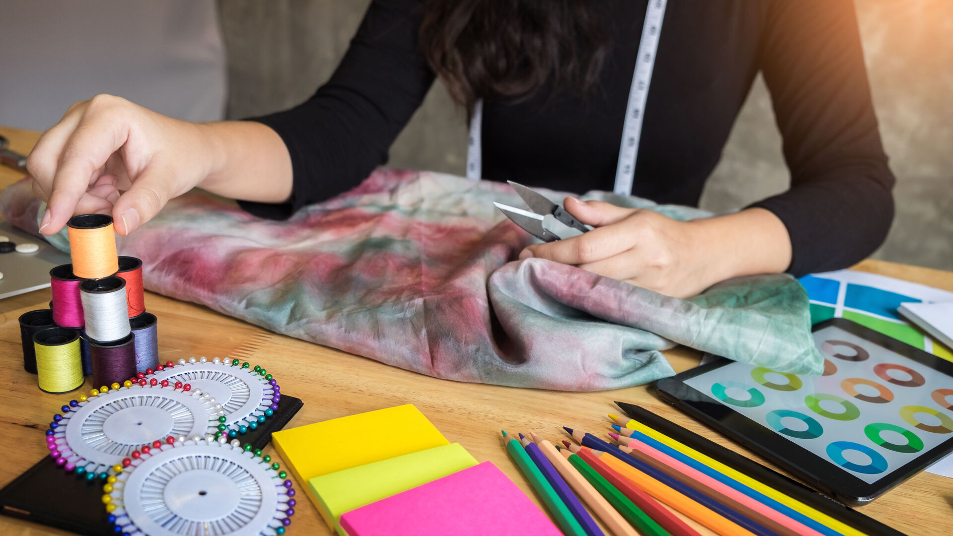 Die Hände einer Frau mit allerlei buntem Näh- und Bastelzubehör am Tisch
