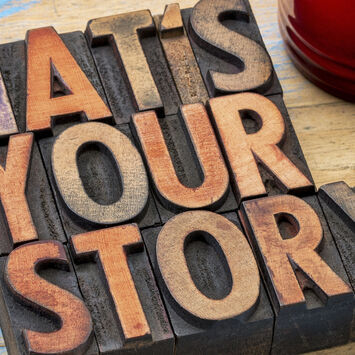 Ein Holzschild mit der Aufschrift "What's your story?" und eine rote Tasse mit Kaffee