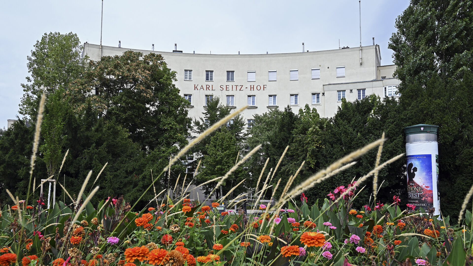 Die Fassade des Karl-Seitz-Hofs vor einer orange-pinken Blumenwiese