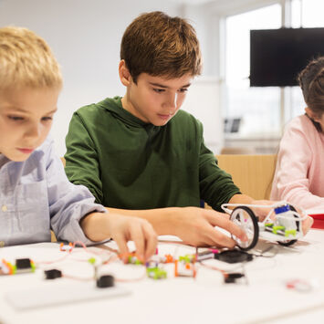 Drei Schüler*innen tüfteln im Workshop an einem kleinen Roboter.