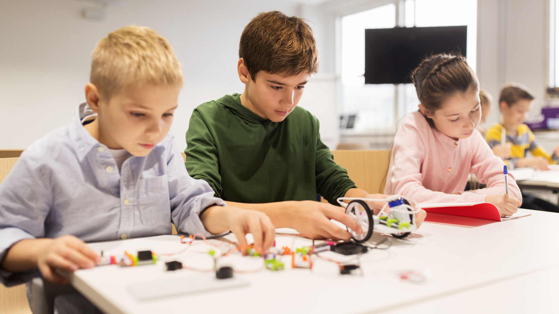 Drei Schüler*innen tüfteln im Workshop an einem kleinen Roboter.