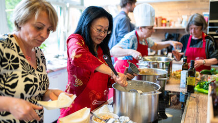 Bewohner*innen beim Kochen in einer Gemeinschaftsküche. Sie sind feierlich angezogen, da es sich um eine Kochbuchpräsentation handelt.