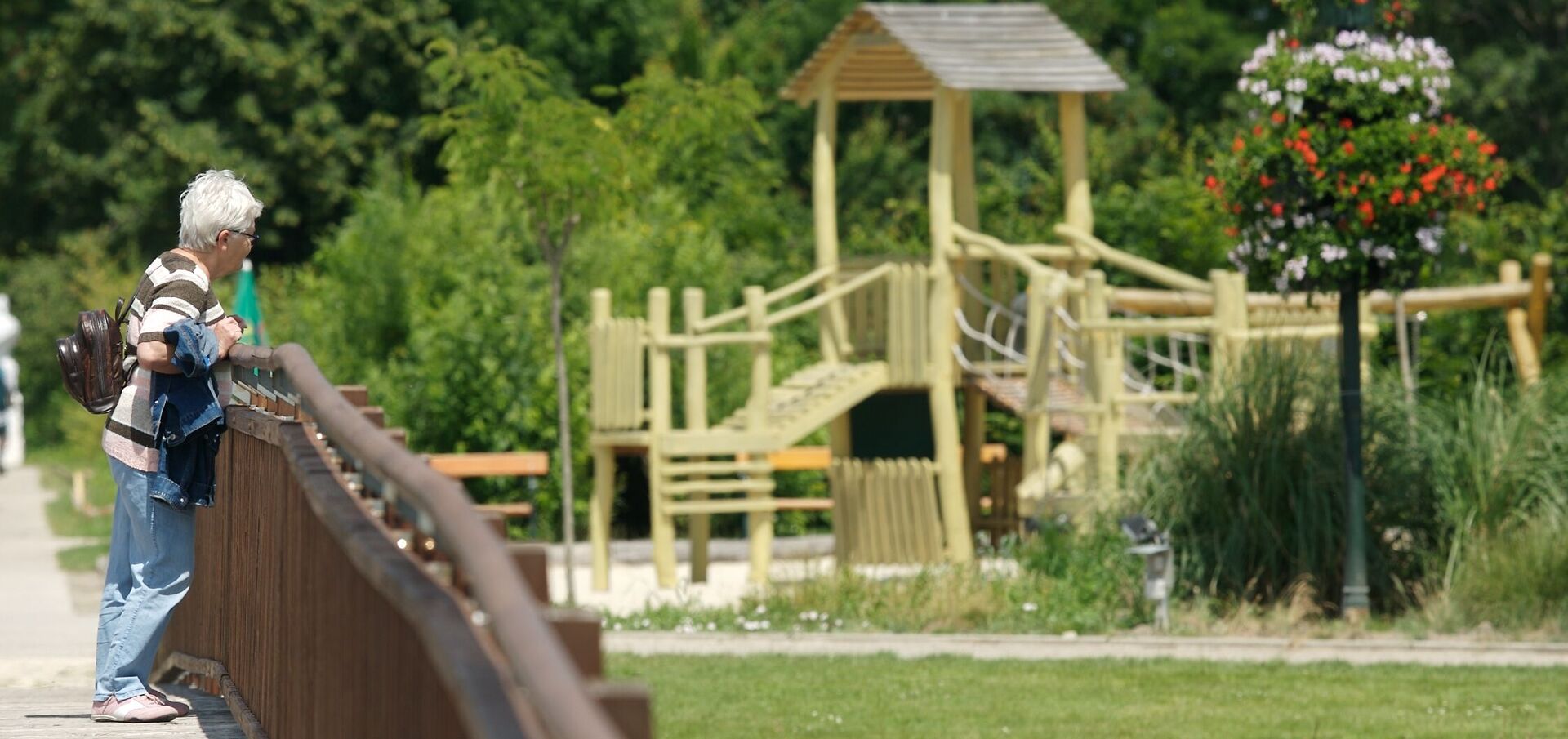 Eine Frau steht auf einer Holzbrücke in den Blumengärten Hirschstetten, im Hintergrund sieht man einen Spielplatz.