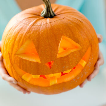 Eine Frau hält einen geschnitzten Halloween-Kürbis in die Höhe.