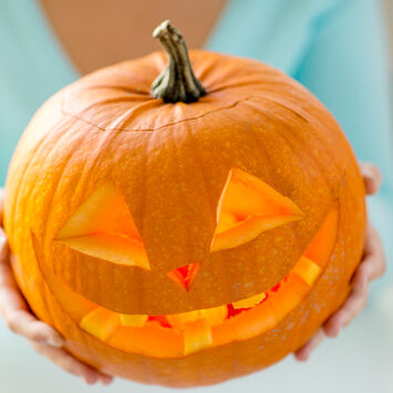 Eine Frau hält einen geschnitzten Halloween-Kürbis in die Höhe.
