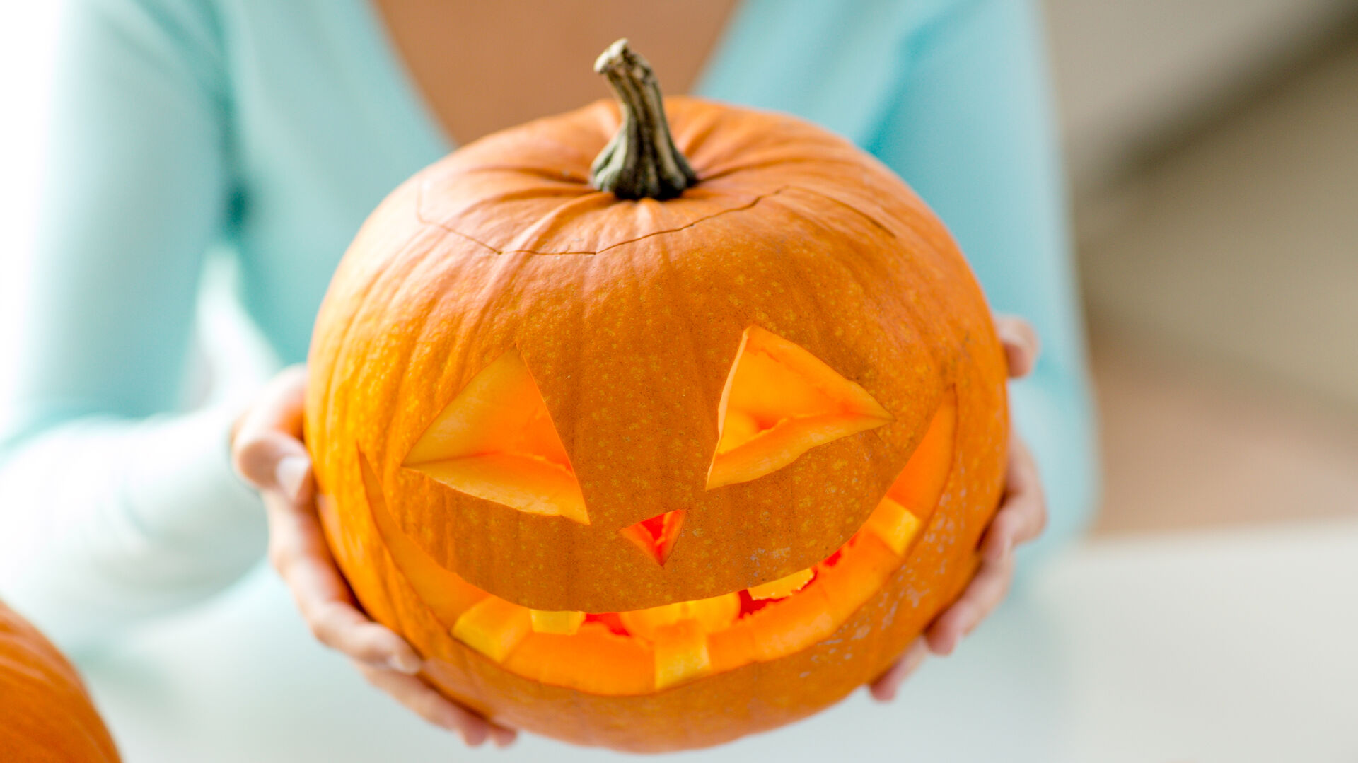 Eine Frau hält einen geschnitzten Halloween-Kürbis in die Höhe.