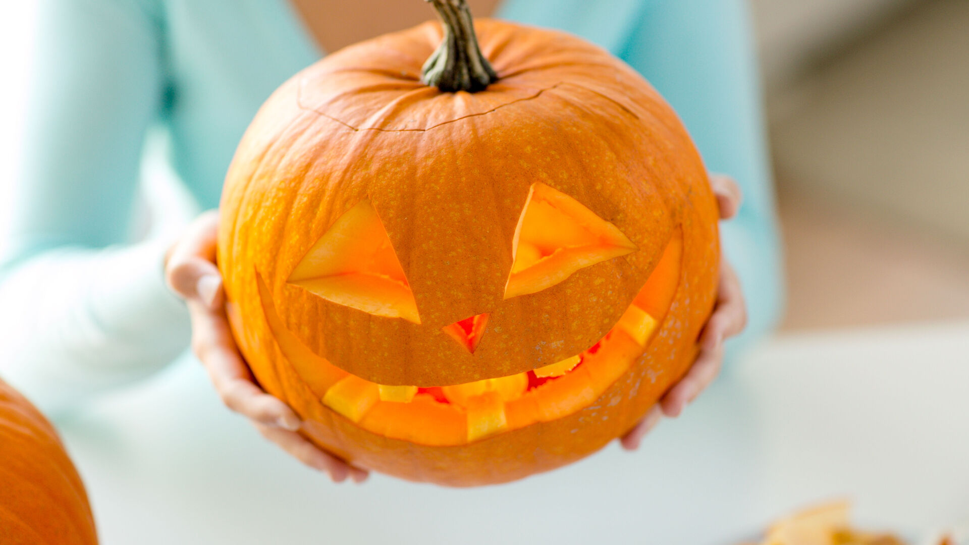 Eine Frau hält einen geschnitzten Halloween-Kürbis in die Höhe.