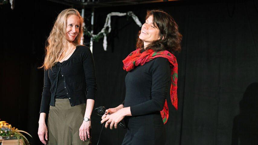 Zwei Personen stehen mit breitem Lächeln nebeneinander. eine davon hat den Kopf etwas nach hinten gebeugt und die Augen geschlossen.