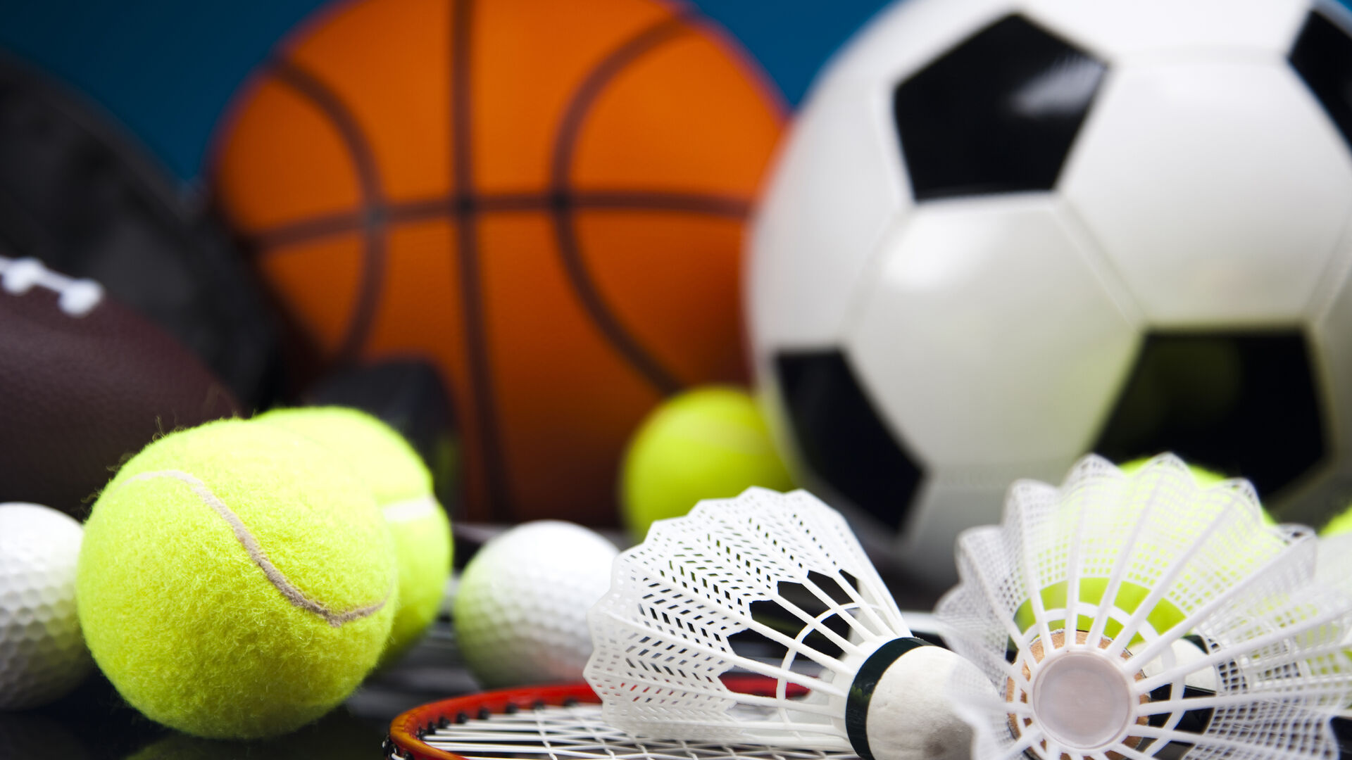 Verschiedene Sportbälle und Federbälle mit einem Badmintonschläger auf dunklem Untergrund