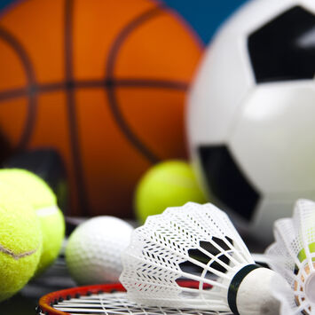 Verschiedene Sportbälle und Federbälle mit einem Badmintonschläger auf dunklem Untergrund
