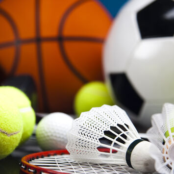 Verschiedene Sportbälle und Federbälle mit einem Badmintonschläger auf dunklem Untergrund