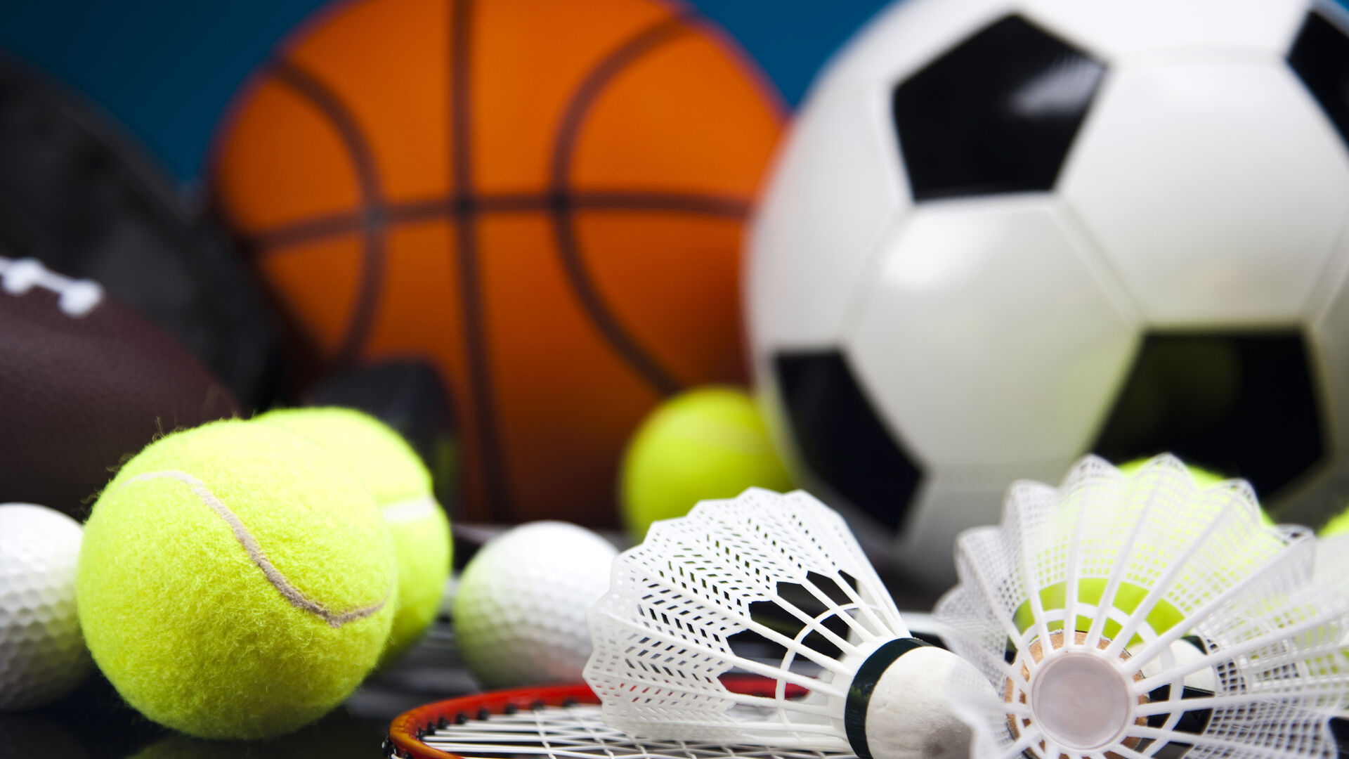 Verschiedene Sportbälle und Federbälle mit einem Badmintonschläger auf dunklem Untergrund
