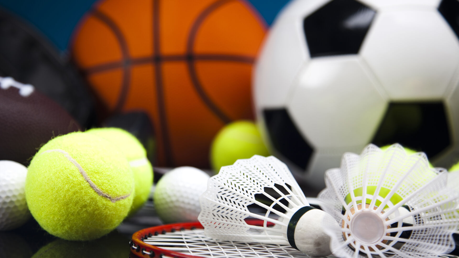 Verschiedene Sportbälle und Federbälle mit einem Badmintonschläger auf dunklem Untergrund