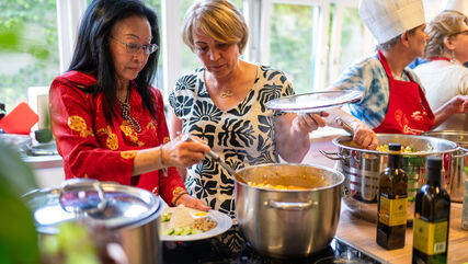Bewohner*innen beim Kochen in einer Gemeinschaftsküche. Sie sind feierlich angezogen, da es sich um eine Kochbuchpräsentation handelt.