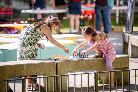 Zwei Mädchen spielen auf einer Parkbank Schach.