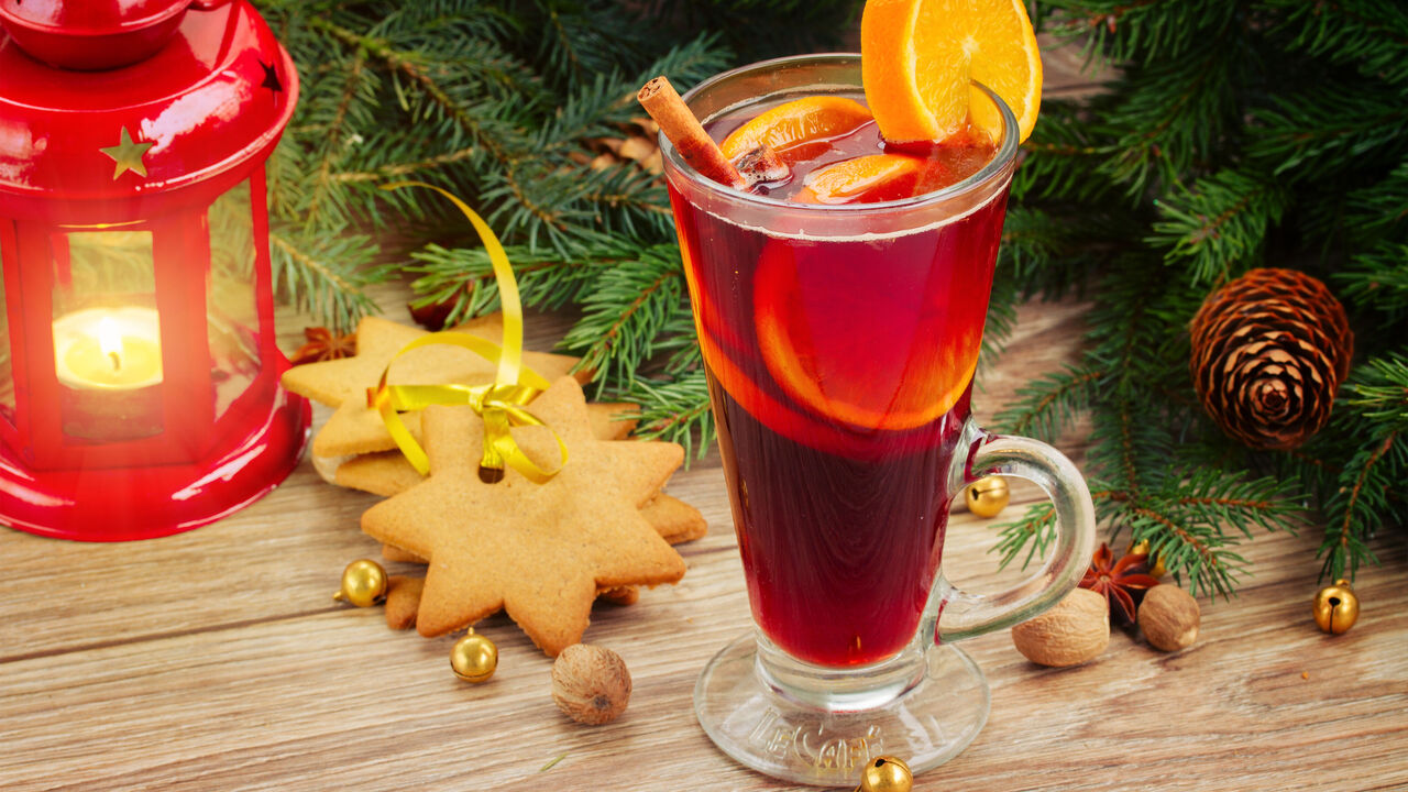 Ein Glas Punsch mit Orangenscheiben und Zimtstange, sternförmige Kekse, eine rote Laterne, Tannenzweige