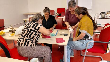 Vier Frauen sitzen um einen Tisch und arbeiten gemeinsam an einem Handarbeitsprojekt mit Stoffen