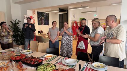 Gruppe von Menschen steht um einen gedeckten Esstisch mit verschiedenen Speisen und lächelt