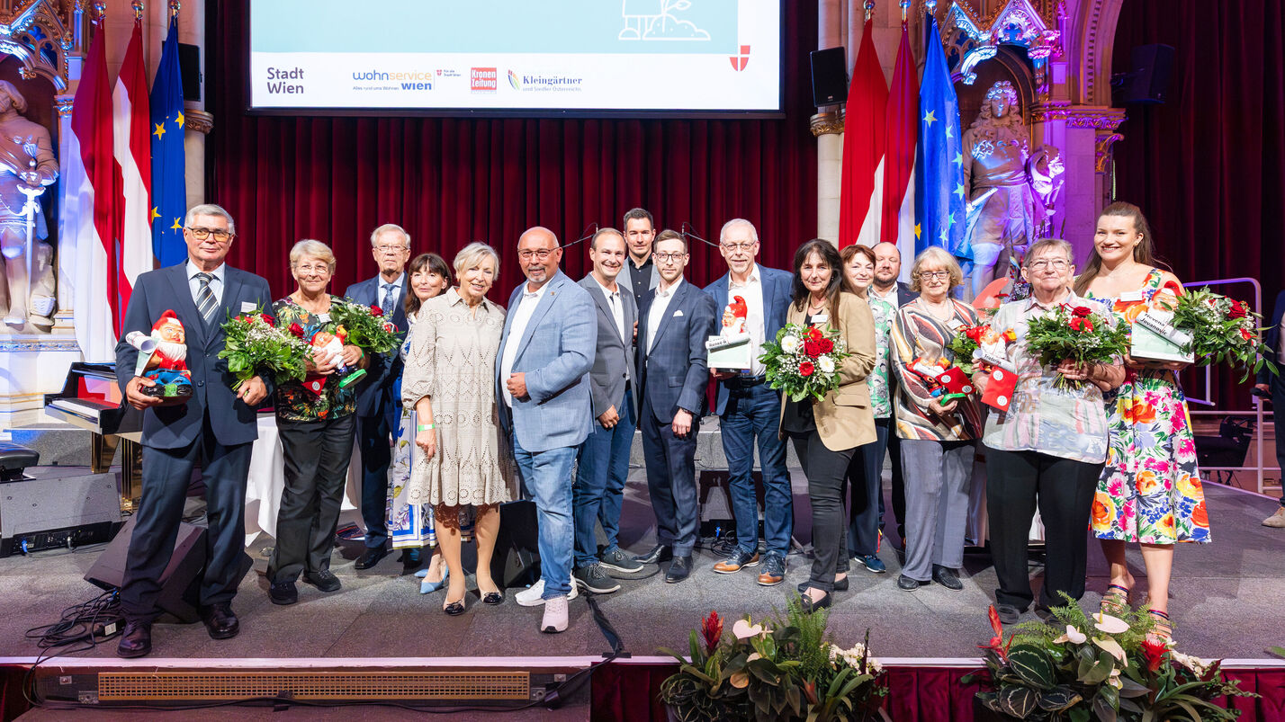 Alle 16 Preisträger*innen des heurigen Kleingartenpreises versammelt auf der Bühne mit Blumensträußen. 