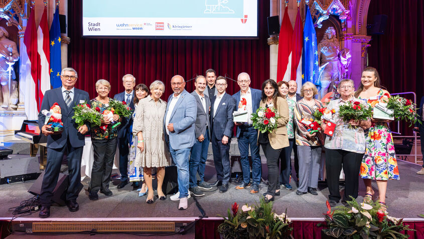 Alle 16 Preisträger*innen des heurigen Kleingartenpreises versammelt auf der Bühne mit Blumensträußen. 