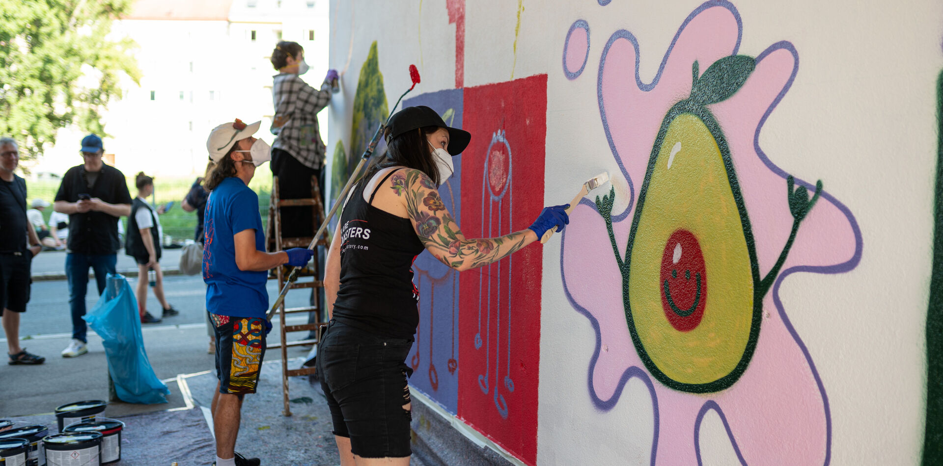 Teilnehmer*innen eines Graffiti-Workshops bemalen eine Hauswand.