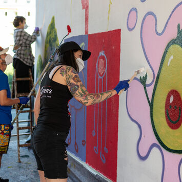 Teilnehmer*innen eines Graffiti-Workshops bemalen eine Hauswand.