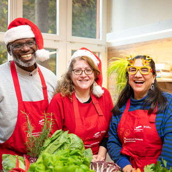 Drei Hobbyköch*innen stehen in einer wohnpartner-Küche und tragen Weihnachtsmützen und -brillen.