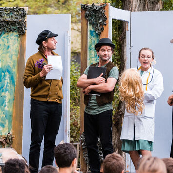 Theater-Schauspieler*innen treten auf einer Freiluftbühne vor Zuschauer*innen auf.