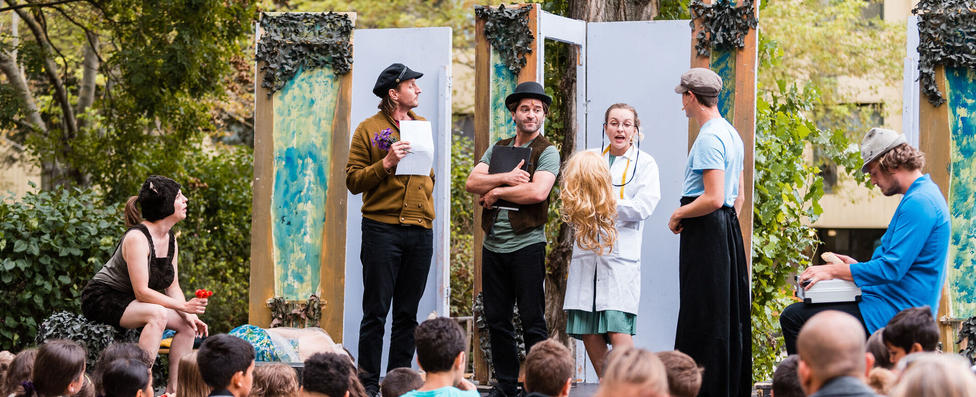 Theater-Schauspieler*innen treten auf einer Freiluftbühne vor Zuschauer*innen auf.