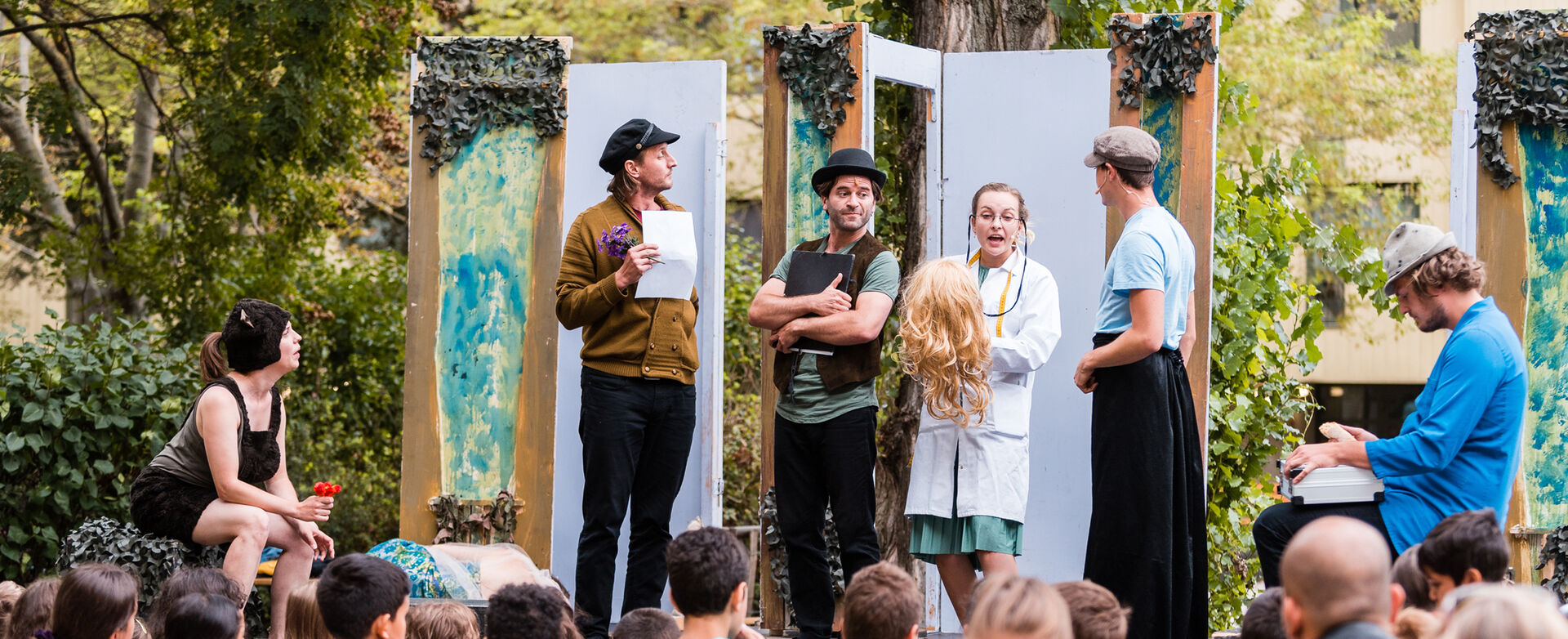 Theater-Schauspieler*innen treten auf einer Freiluftbühne vor Zuschauer*innen auf.
