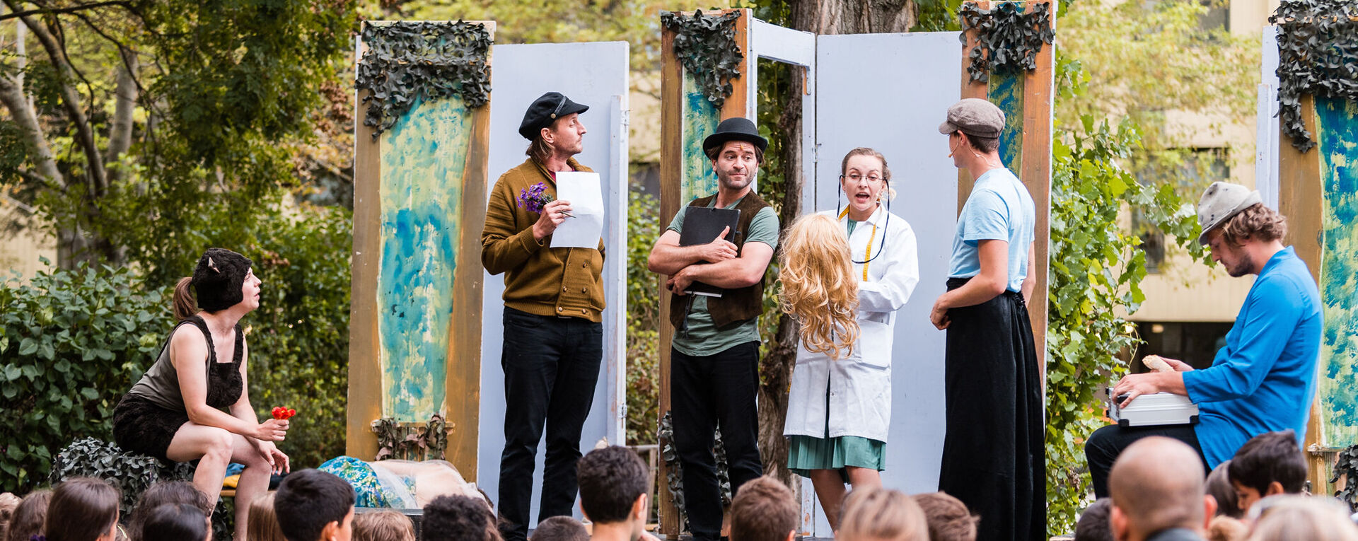 Theater-Schauspieler*innen treten auf einer Freiluftbühne vor Zuschauer*innen auf.