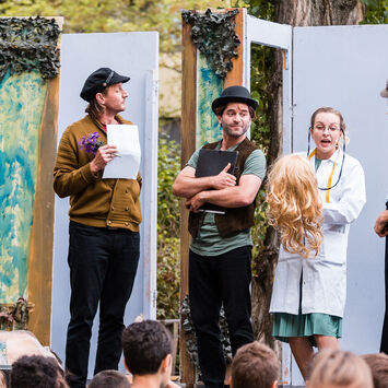 Theater-Schauspieler*innen treten auf einer Freiluftbühne vor Zuschauer*innen auf.