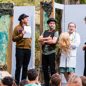 Theater-Schauspieler*innen treten auf einer Freiluftbühne vor Zuschauer*innen auf.