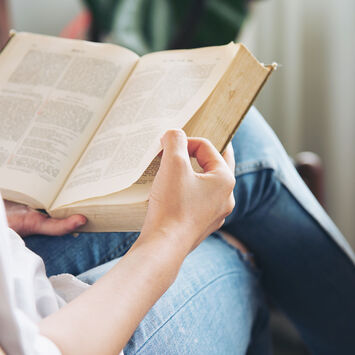 Eine Frau sitzt mit übereinander geschlagenen Beinen auf einem Sessel und liest ein Buch.