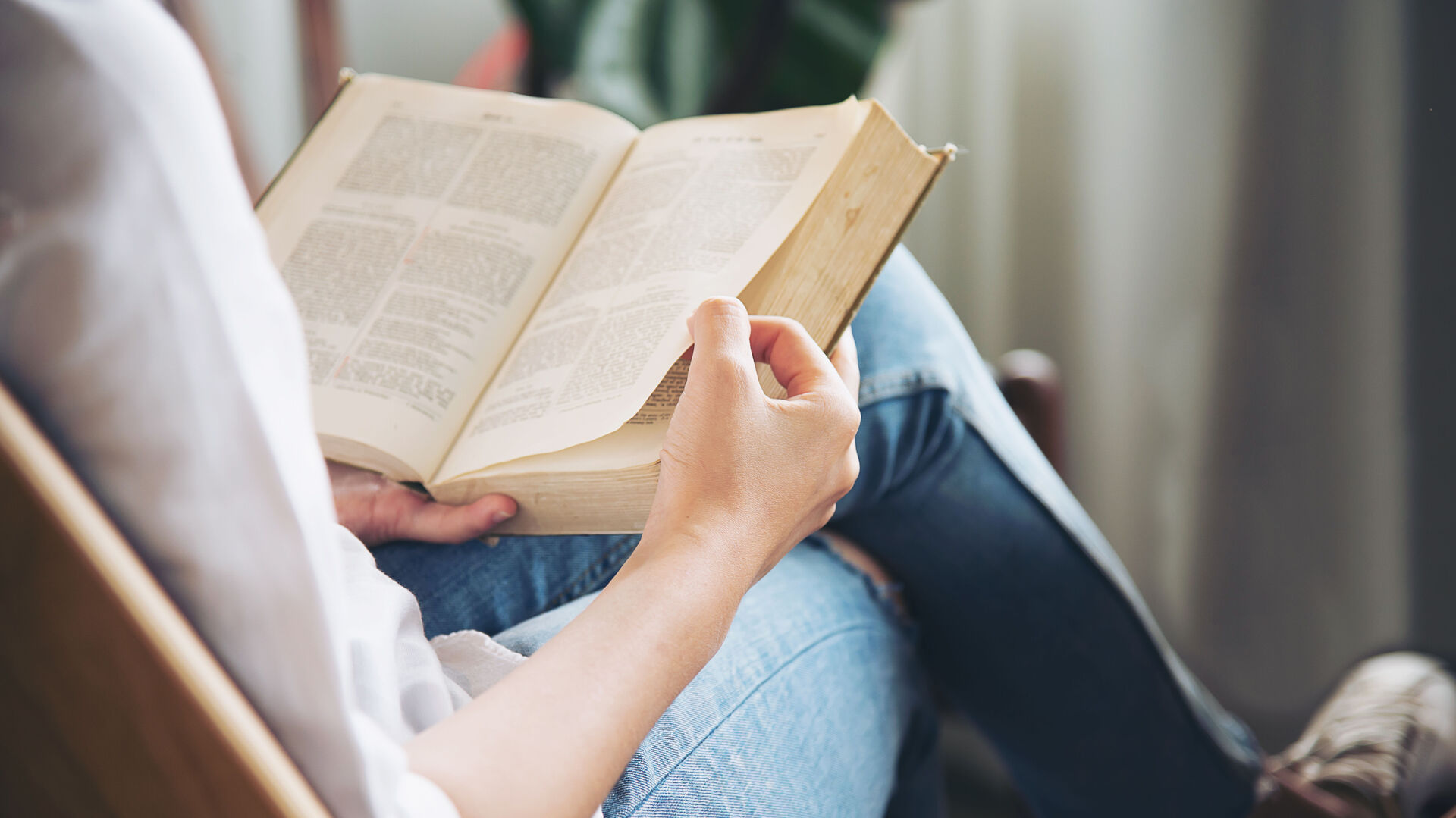 Eine Frau sitzt mit übereinander geschlagenen Beinen auf einem Sessel und liest ein Buch.