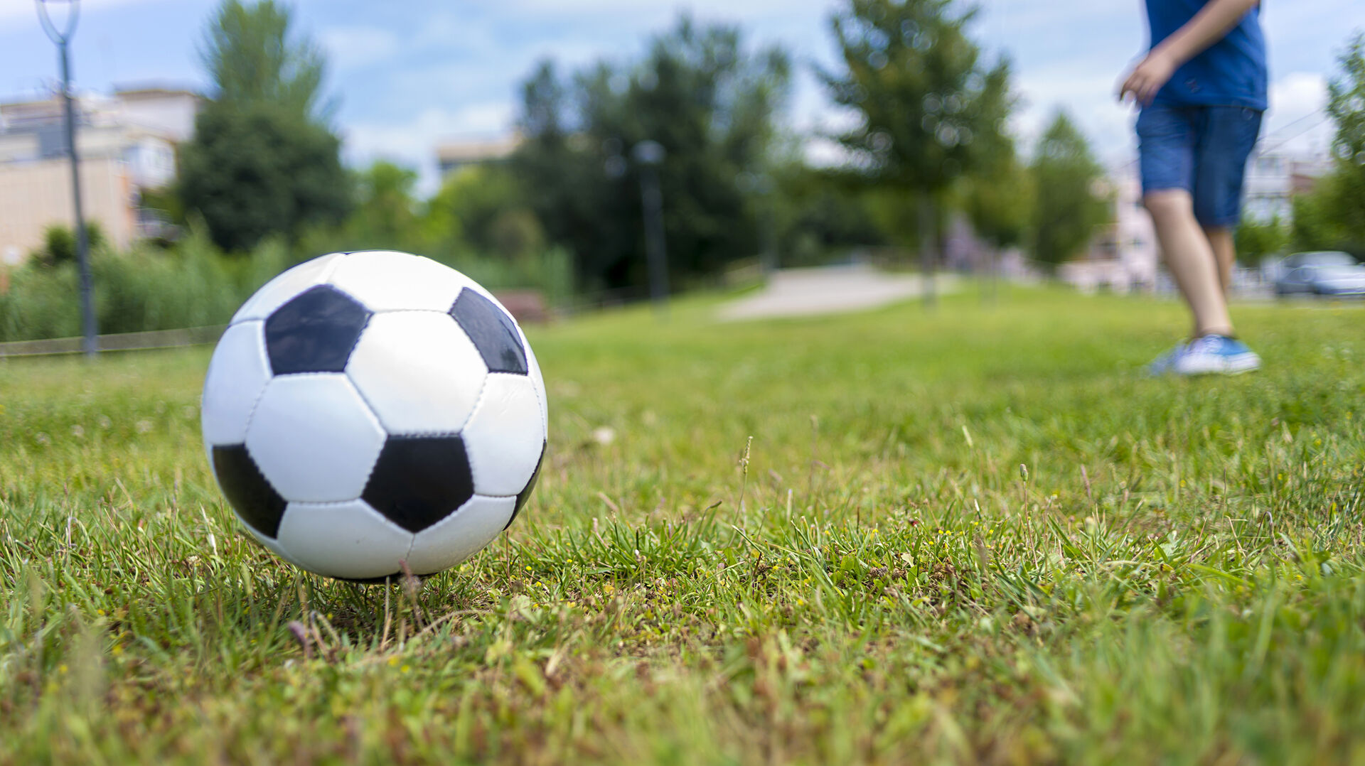 Schwarz-weißer Fußball auf einem Rasen mit unscharfem Hintergrund und einer Person in Shorts und Turnschuhen