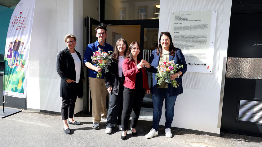 Wiener Wohnen Direktorin Karin Ramser, Bezirksvorsteher Michael Luxenberger und Vizebürgermeisterin und Wohnbaustadträtin Kathrin Gaál mit frisch eingezogenen Bewohnerinnen stehen vor dem Eingang des Gemeindebau NEU in der Schönbrunnerstraße. Kathrin Gaál überreicht der neuen Mieterin symbolisch ihren Wohnungsschlüssel. Sie hält dabei auch einen bunten Blumenstrauß in der Hand, ebenso wie der Bezirksvorsteher von Margareten