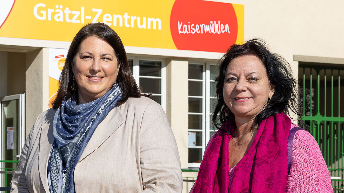 Viezbürgermeisterin Gall steht mit wohnpartner-Bereichsleiterin Claudia Huemer vor einem Gebäude. Über dem Eingangsportal ist der Schriftzug Grätzl-Zentrum Kaisermühlen zu lesen..