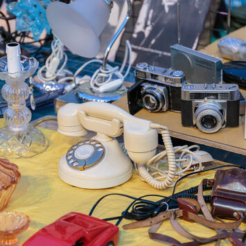 Flohmarkt-Ware auf einem Tisch: alte Telefone, Fotoapparate, Lampen, etc.