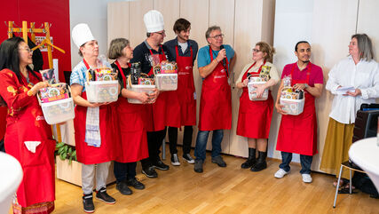 Stolze Bewohner*innen in roten Kochschürzen haben gerade einen kleinen Geschenkkorb mit Kochbuch erhalten