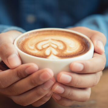 Zwei Hände halten eine Tasse Kaffee mit Milchschaum und Herzmuster