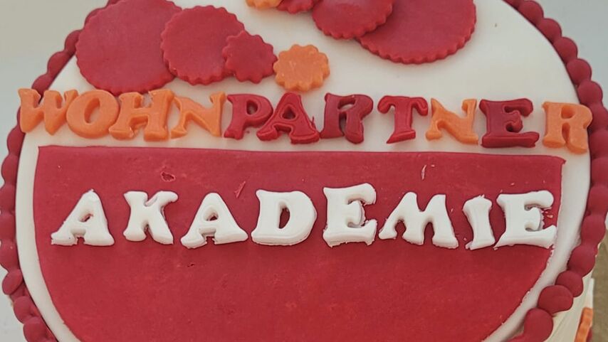 Runde Torte mit rotem Fondant und den Worten 'WOHNPARTNER AKADEMIE' aus Zuckerschrift auf der Oberseite