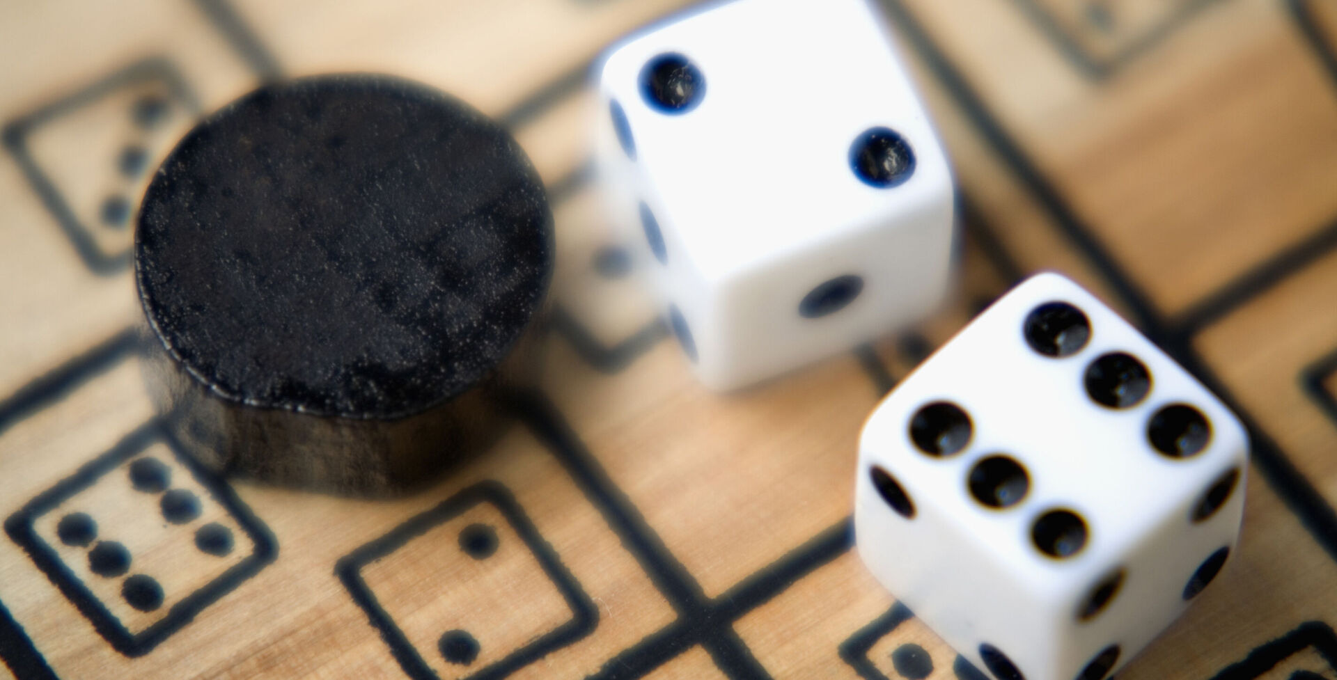 Zwei Würfel und ein Spielstein auf einem Spielebrett aus Holz