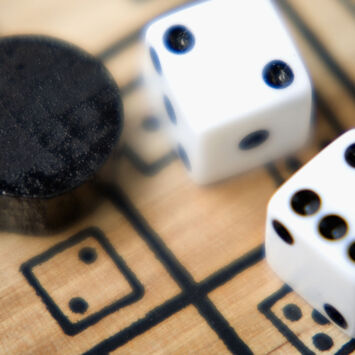 Zwei Würfel und ein Spielstein auf einem Spielebrett aus Holz